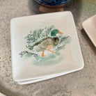 Square ceramic plate with a duck illustration on a gray surface