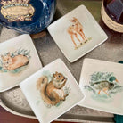 Set of ceramic plates with animal illustrations on a table with a bottle of whisky in the background.
