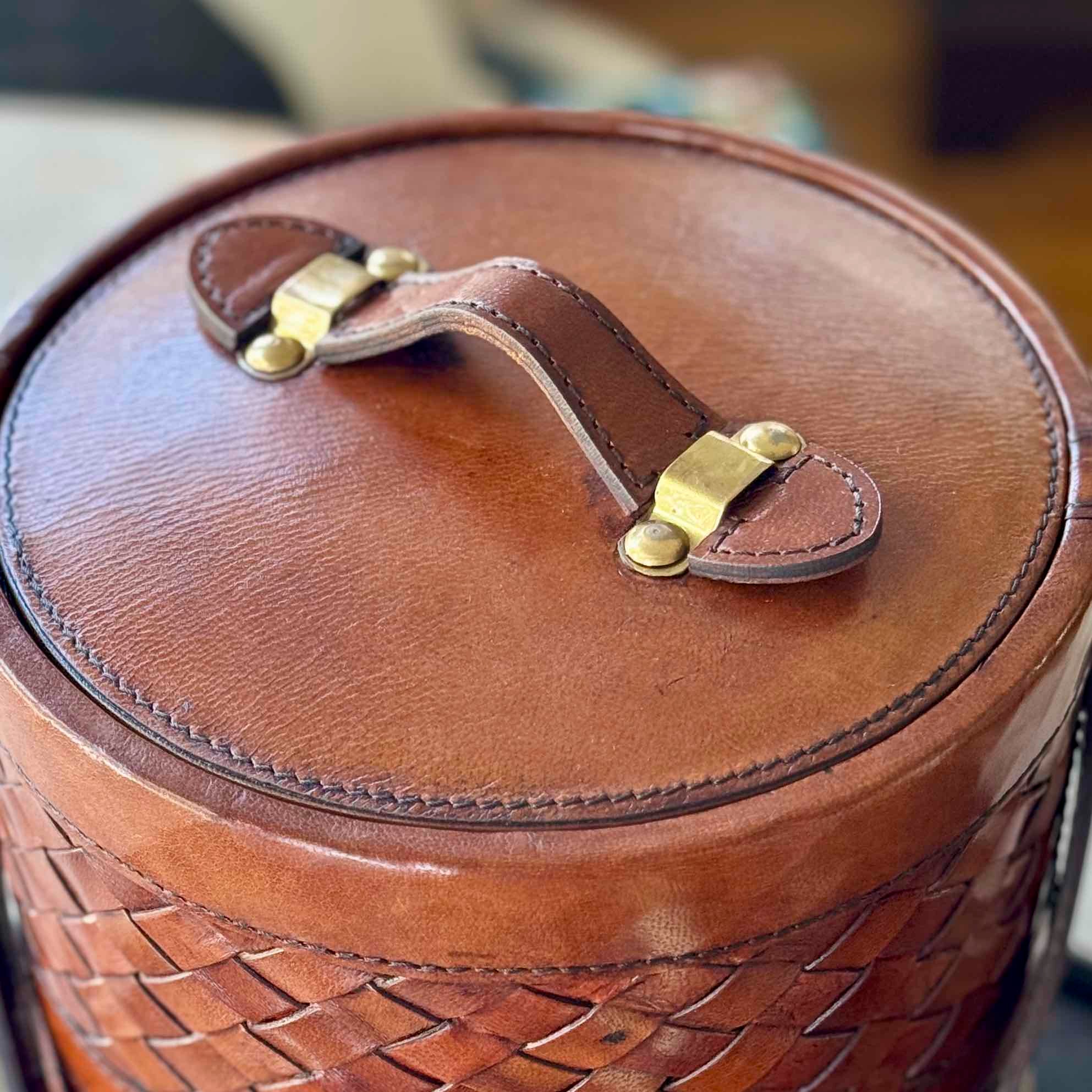 Close-up of a brown leather basket with braided handle and gold clasp.