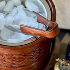 Brown woven ice bucket with leather handle and ice cubes inside