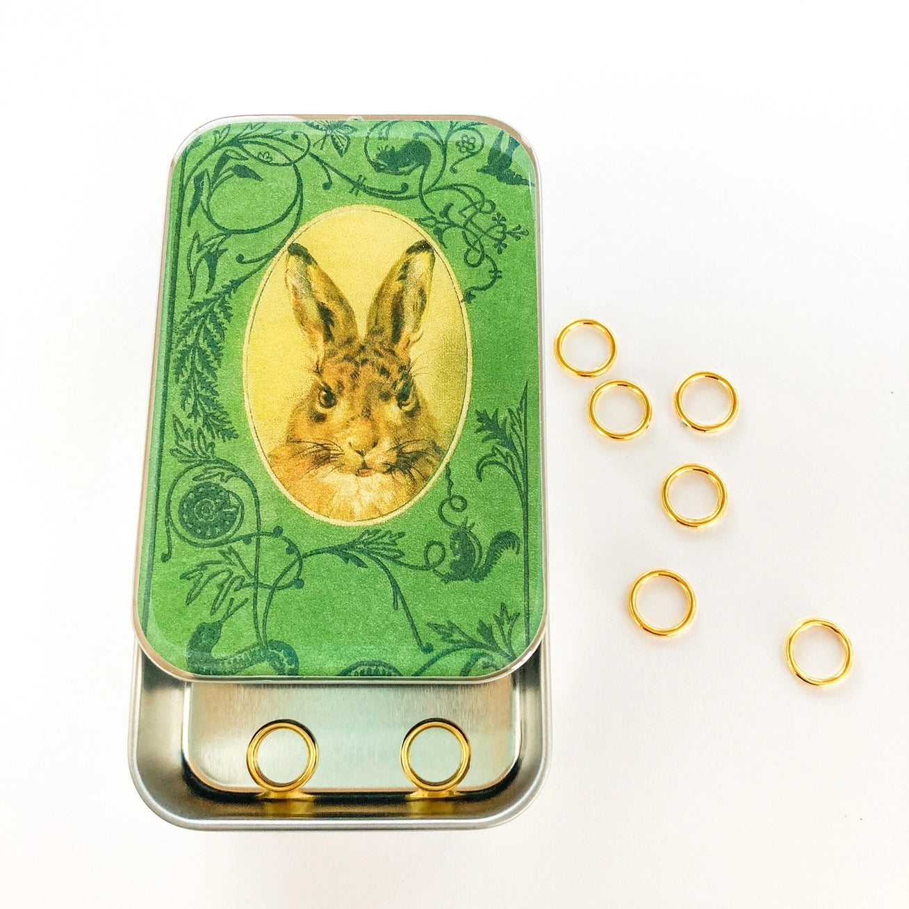 Green tin with rabbit illustration and gold rings on a white background