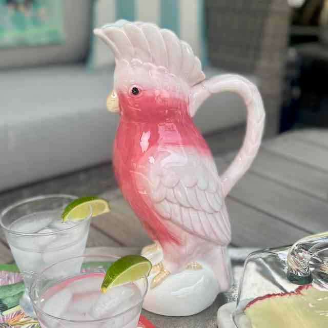Pink and white parrot-shaped pitcher on a table with drinks and lime wedges.