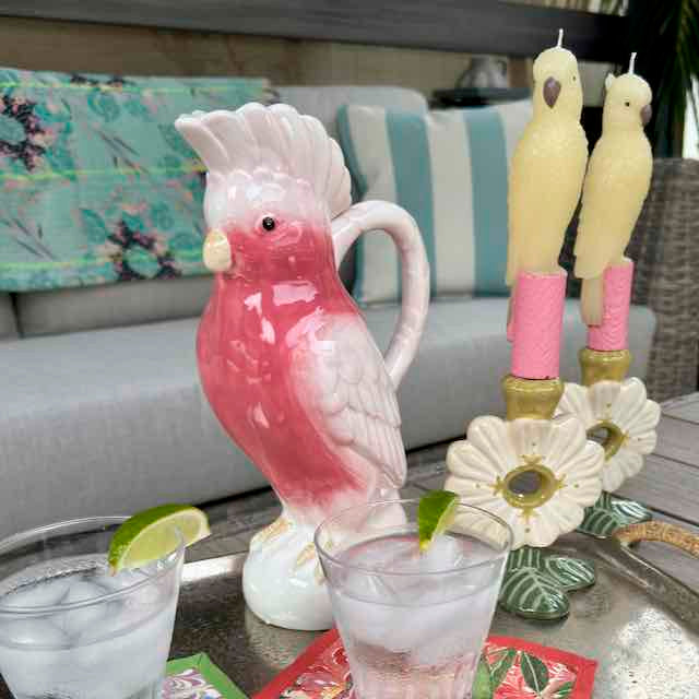 Pink parrot-shaped pitcher with candles on a tray with drinks and lime wedges.