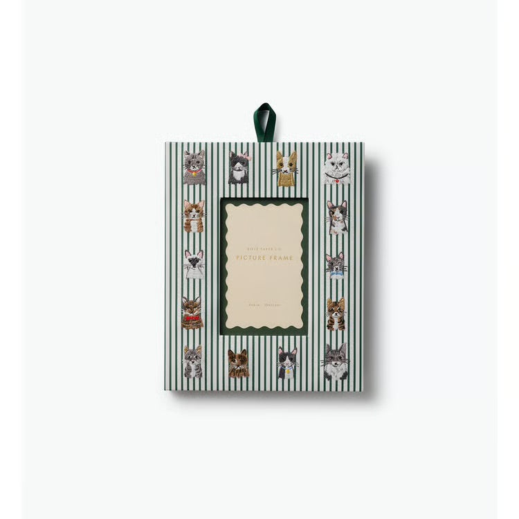 A decorative picture frame with a hanging ribbon, featuring a green and white striped pattern with various cat illustrations around a central cream-colored label area.
