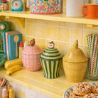 Colorful ceramic jars on a yellow tiled kitchen counter with various kitchen items.