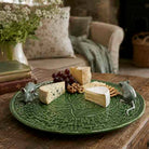 Green decorative plate with cheese, grapes, and cookies on a wooden table.