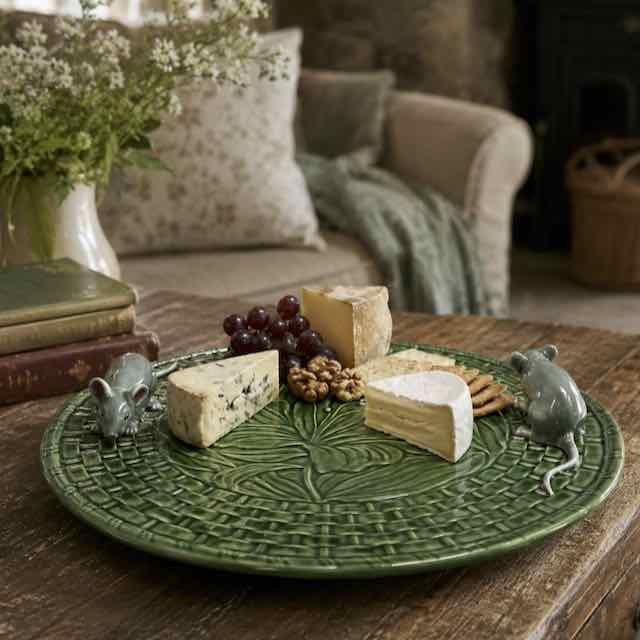 Green decorative plate with cheese, grapes, and cookies on a wooden table.